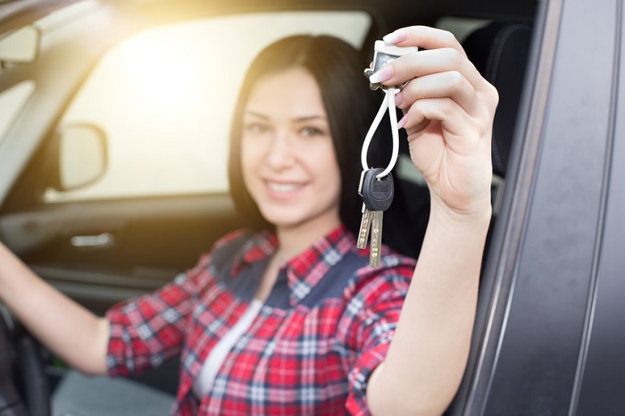 Image of a young woman holding up her car keys while seated in a new sedan.